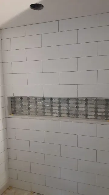 A custom shower tile installation featuring white subway tiles and a horizontal recessed niche with geometric mosaic accent tiles.