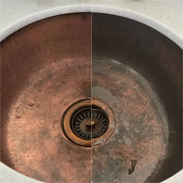 A dirty, rusted kitchen sink with some water dripping and debris at the bottom.