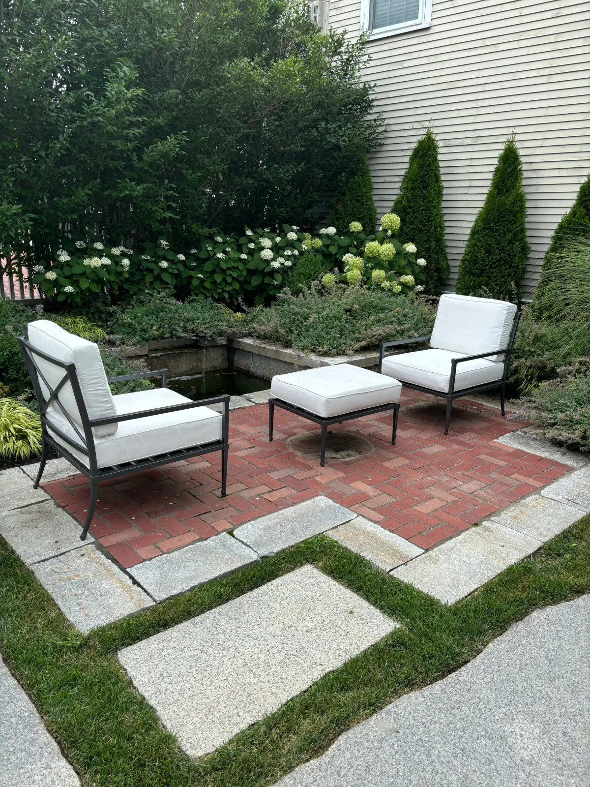 A bespoke granite fountain is the focus of this small space courtyard garden in Newburyport. A brick and reclaimed granite patio with surrounding gardens and grass joints create a classical setting at this complete landscape transformation.