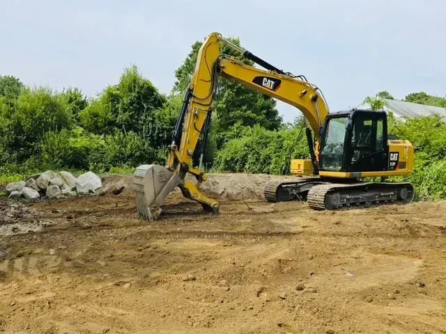 Yellow excavator working on a dirt site with trees in the background