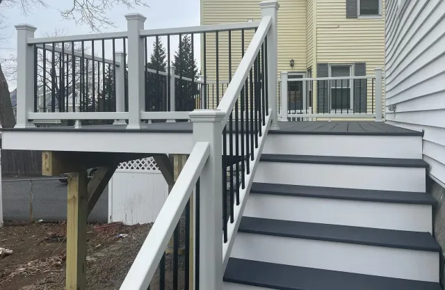 A deck with stairs leading up to it and a house in the background.