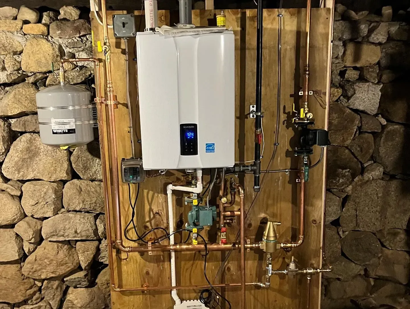 A white water heater is mounted to a wall next to copper pipes.