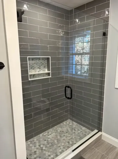A bathroom with gray tiles and a walk-in shower with a glass door.