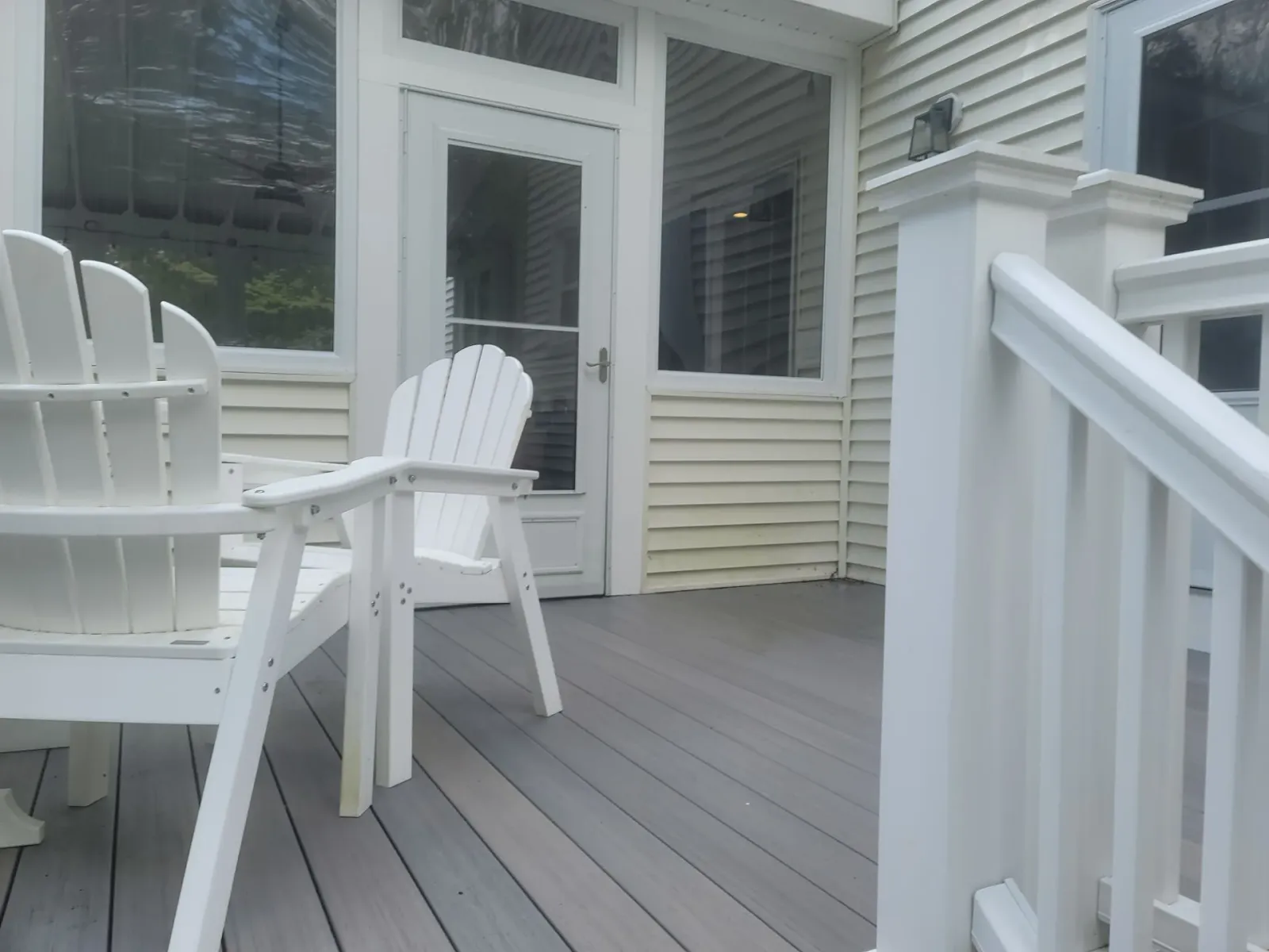 White patio chairs on a gray deck beside a beige house and sliding glass door