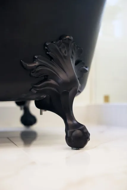 Close-up of a black decorative clawfoot on a vintage-style bathtub or furniture, with a curved ornate design, set on a hard tile floor in a bright room.