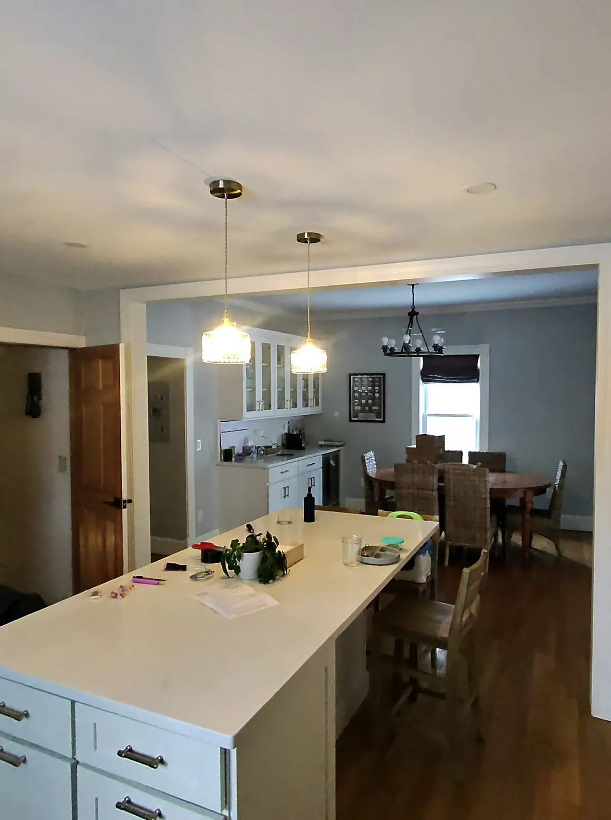 Wide view of a residential kitchen and dining area with a white kitchen island, pendant lights, and hardwood floors in Wellesley, Massachusetts.