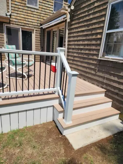 Back steps with white railing leading to a wooden deck beside a shingled house