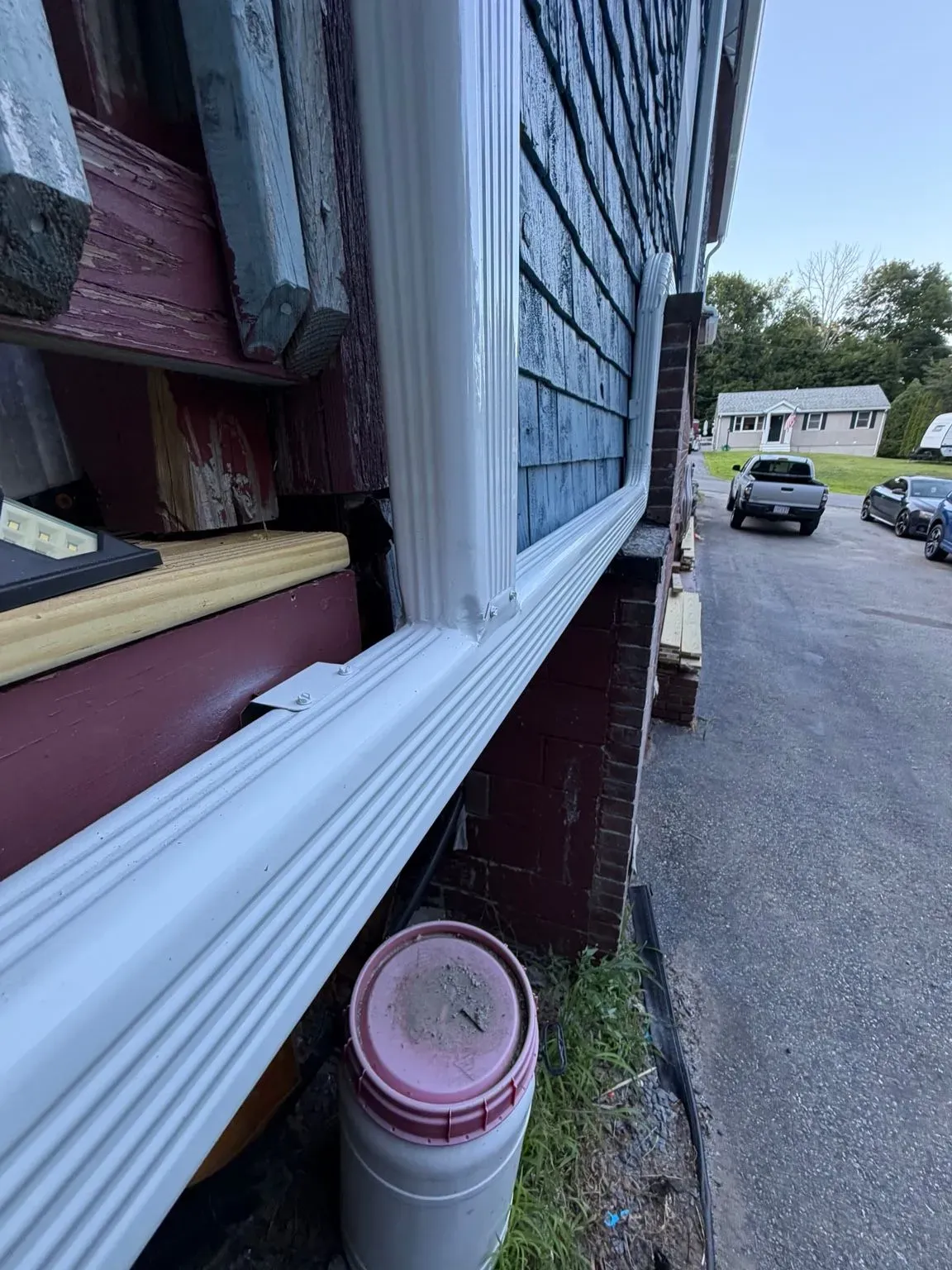 House exterior with white siding, a window, and a driveway with parked cars in the background