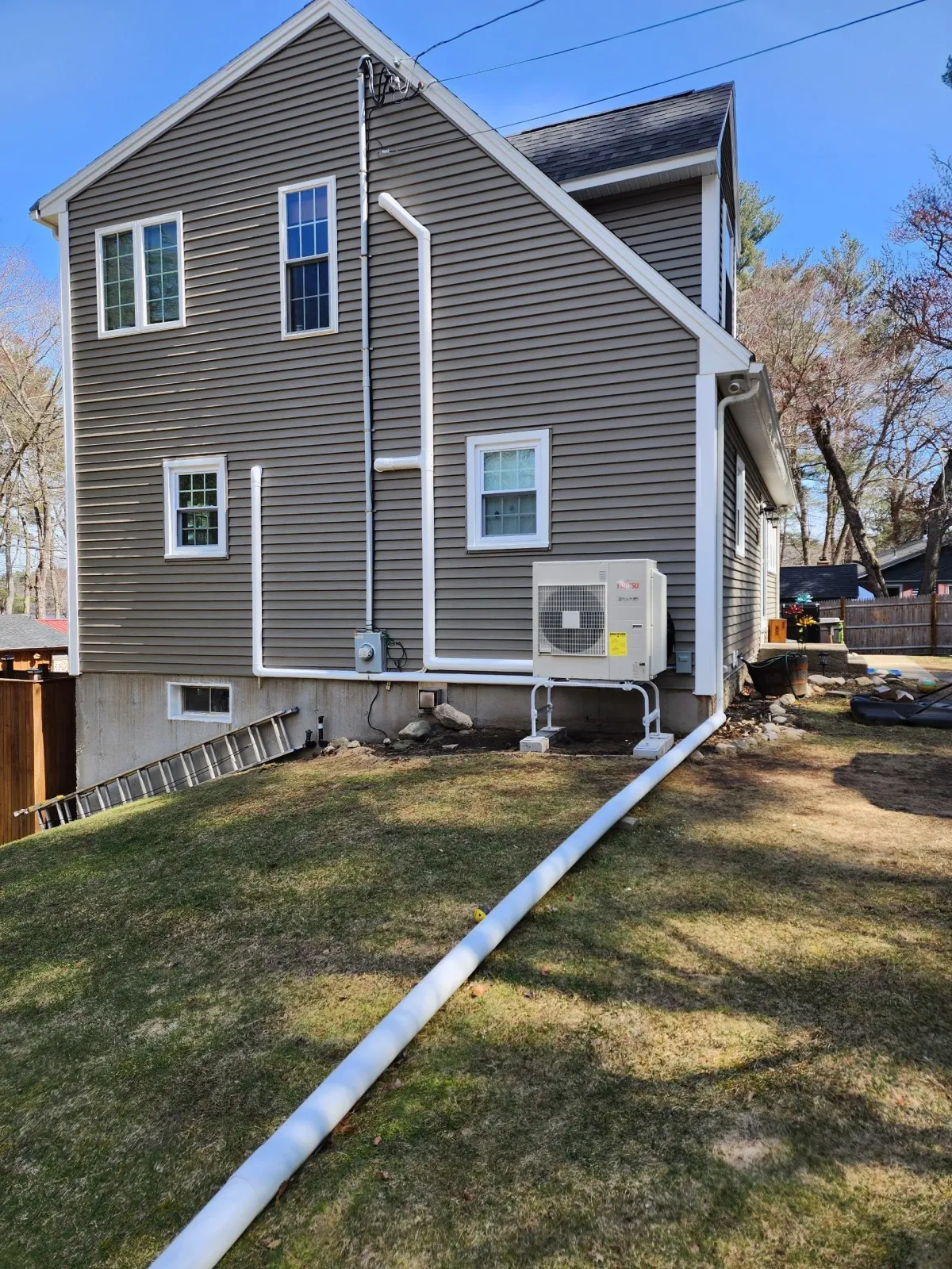 Side view of a gray house with white trim, windows, and downspouts in a grassy yard.