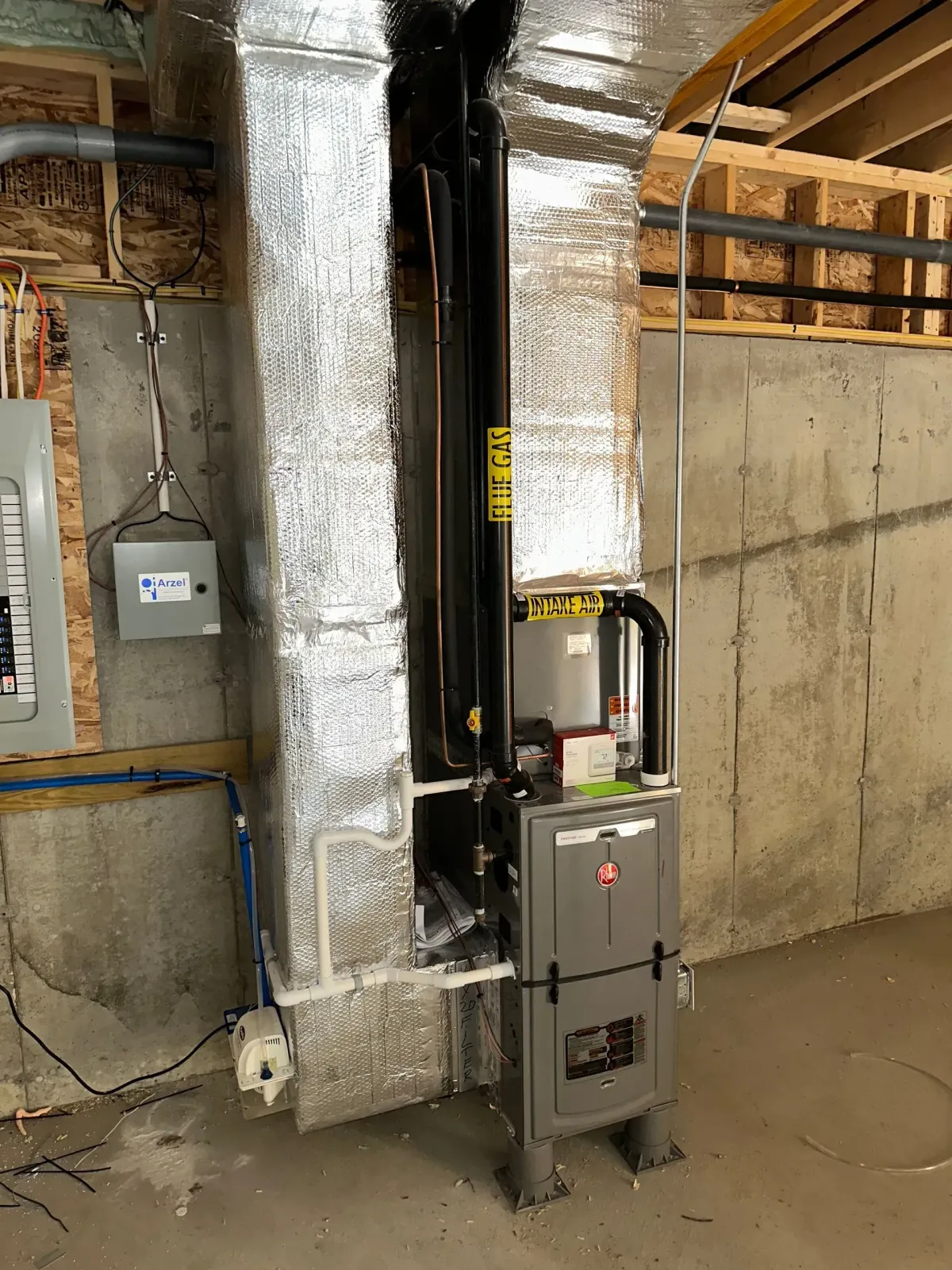 Industrial basement with insulated HVAC ducting, furnace unit, and electrical panel against concrete wall