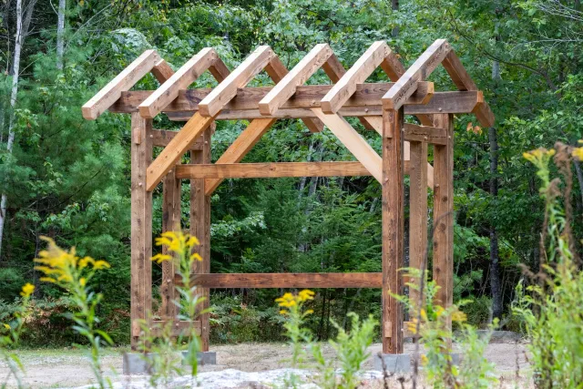 A wooden pergola frame under construction in a forested area.