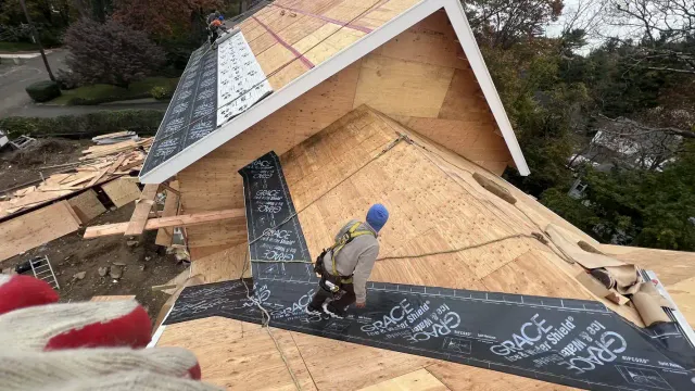 Roofers installing Grace Ice and Water Shield underlayment on a plywood roof deck