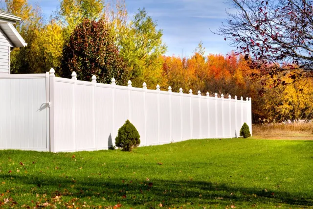 White vinyl fence beside a green lawn with colorful autumn trees in the background