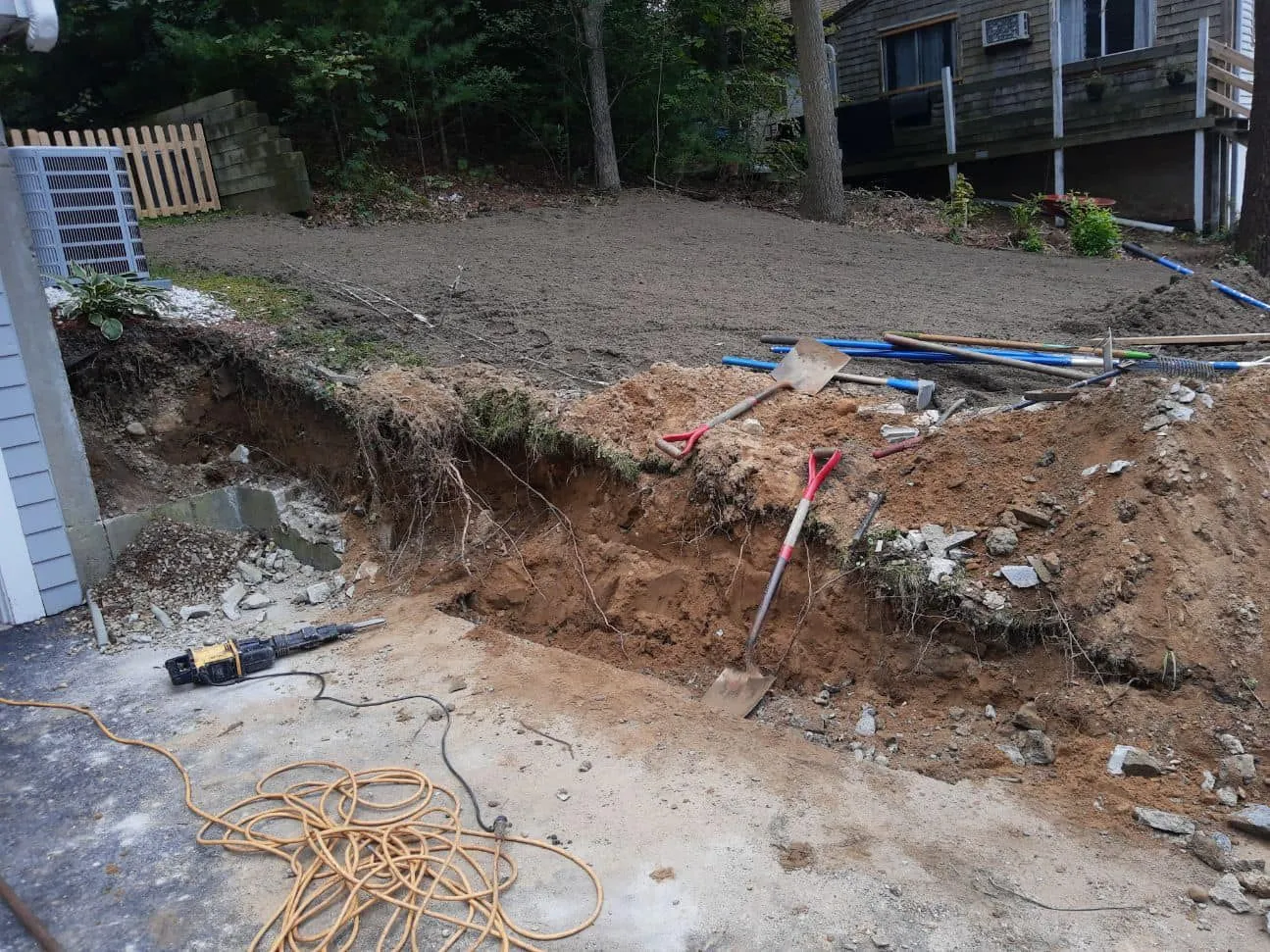 Excavation site with exposed earth, tools, and a partially built fence next to a house.