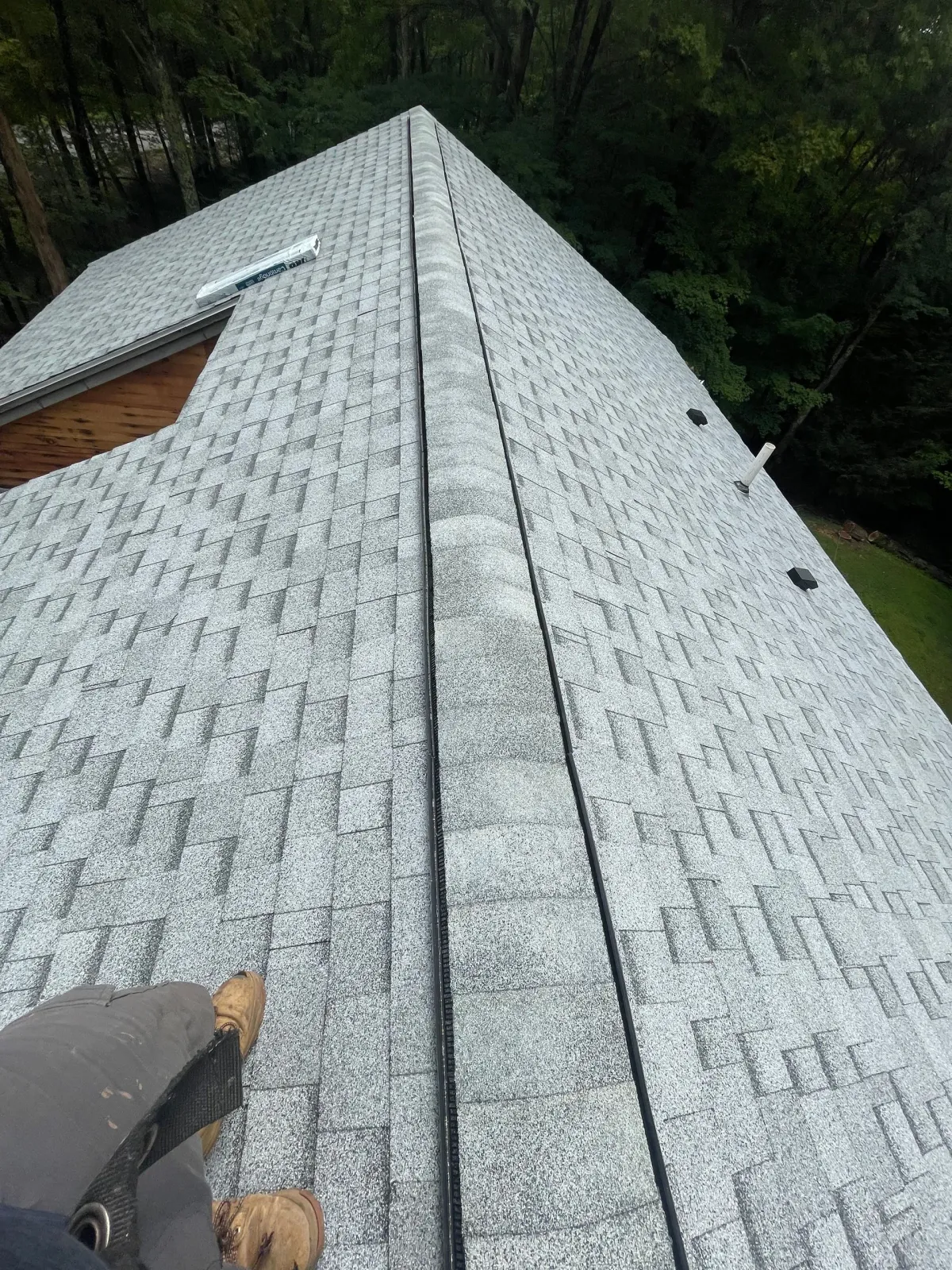 Roofing shingles being installed on a steep, gray roof with trees in the background