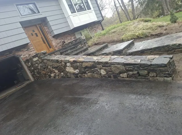Natural stone wall with bluestone caps running along a driveway
