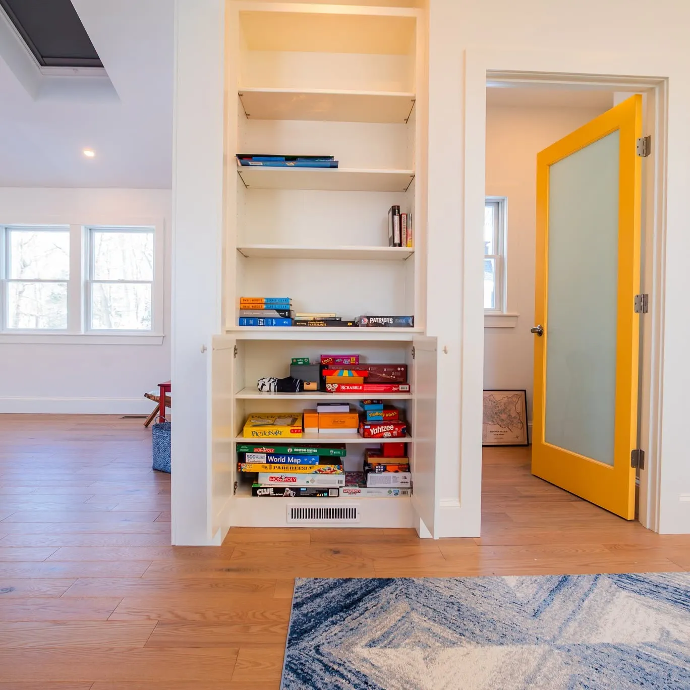 Built-in bookcase and game storage beside a yellow glass-panel door