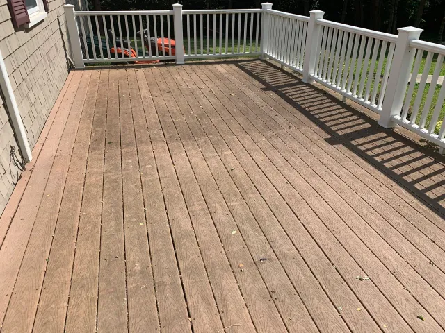 A wooden deck with a white railing and a white fence.