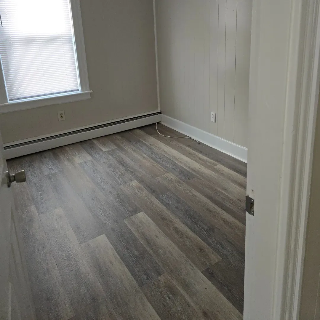 Gray and beige vinyl plank flooring in empty bedroom with shiplap accent wall by Link Services Pro in Worcester, MA
