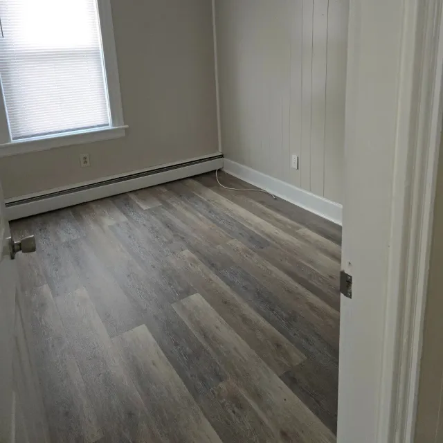 Gray and beige vinyl plank flooring in empty bedroom with shiplap accent wall by Link Services Pro in Worcester, MA