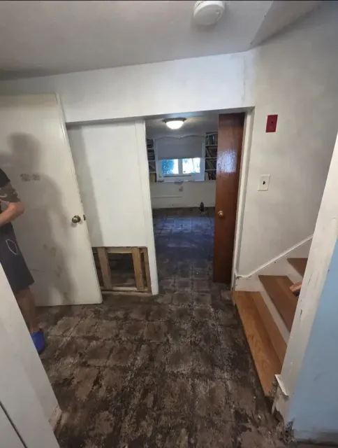 Small hallway with worn flooring, white walls, a doorway to another room, and a staircase on the right.