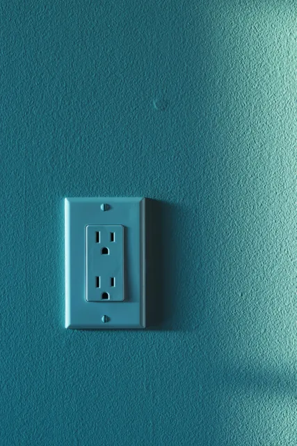 A close-up of a single electrical outlet mounted on a textured light teal wall.