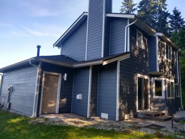 Blue-gray two-story house with a covered porch and unfinished exterior trim under a bright sky