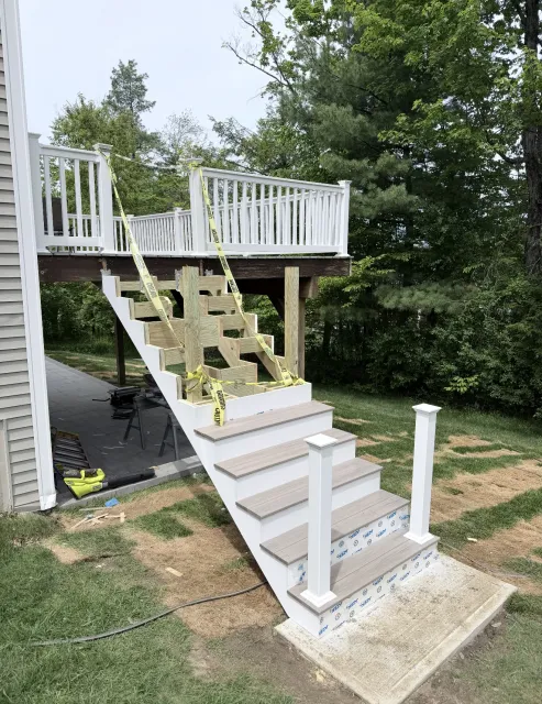 Exterior staircase with white railings and planter boxes leading to a raised deck in a yard
