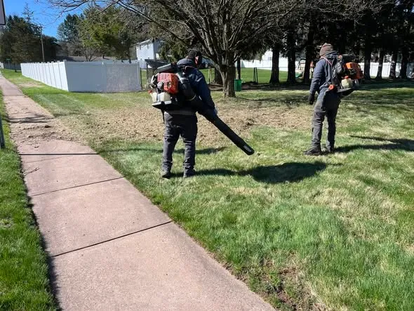 Gardner and Sons crew clearing leaves and winter debris from a residential lawn