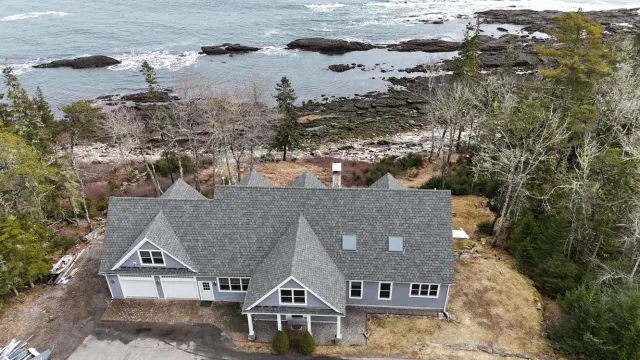 House with gray roof, light blue siding near rocky ocean