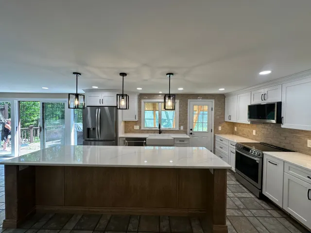 Modern kitchen with large island, pendant lights, stainless appliances, white cabinets, and tile floor.
