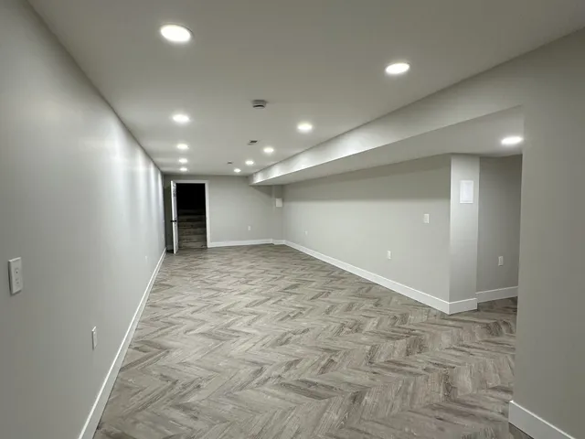 Finished basement in Madison Connecticut with herringbone luxury vinyl plank flooring, white walls, recessed LED lighting, and a soffit built around ductwork