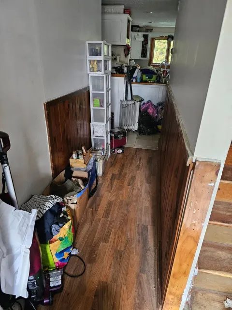 A hallway with wooden floors and stairs in a house filled with lots of stuff.