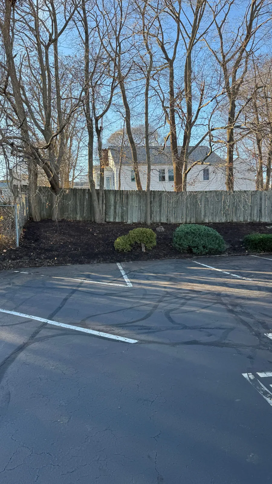 Parking lot with white lines, fence, trees, and a house in the background.