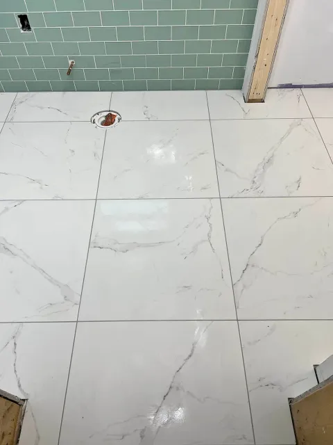 A bathroom floor with white tiles and green subway tiles.
