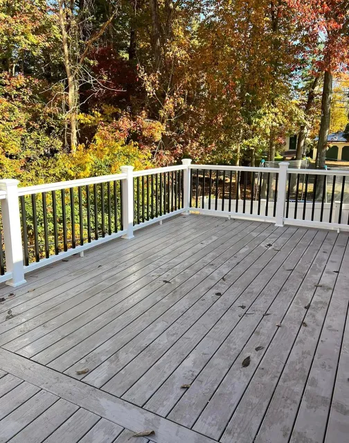 A wooden deck with a white railing and trees in the background