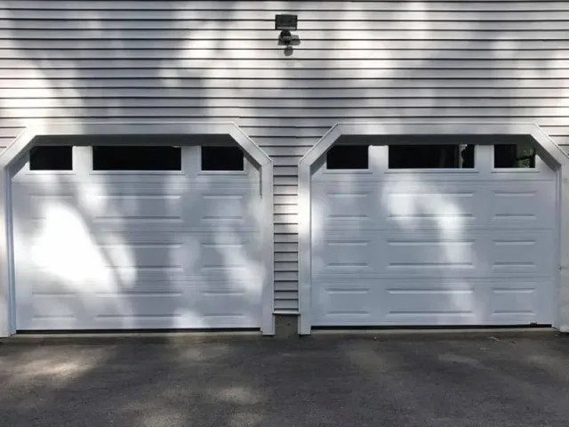 A pair of white garage doors are sitting next to each other on the side of a house.