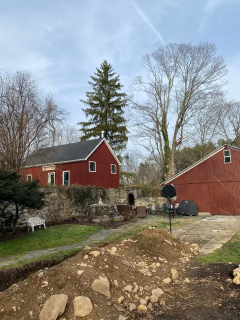 A red barn is sitting in the middle of a dirt field next to a house.
