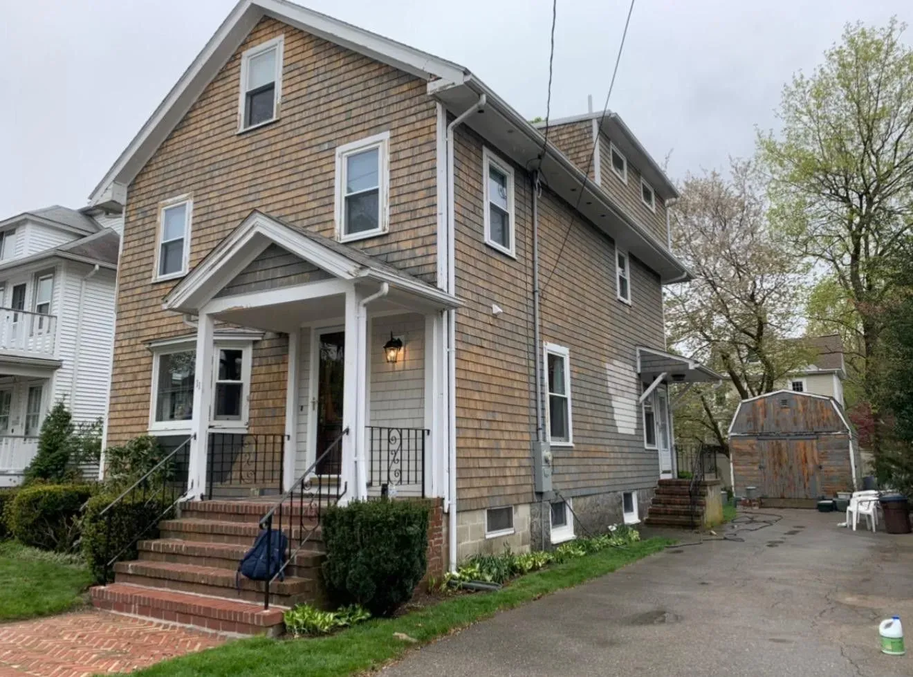 Brick two-story house with front porch and driveway, viewed from the side on a cloudy day