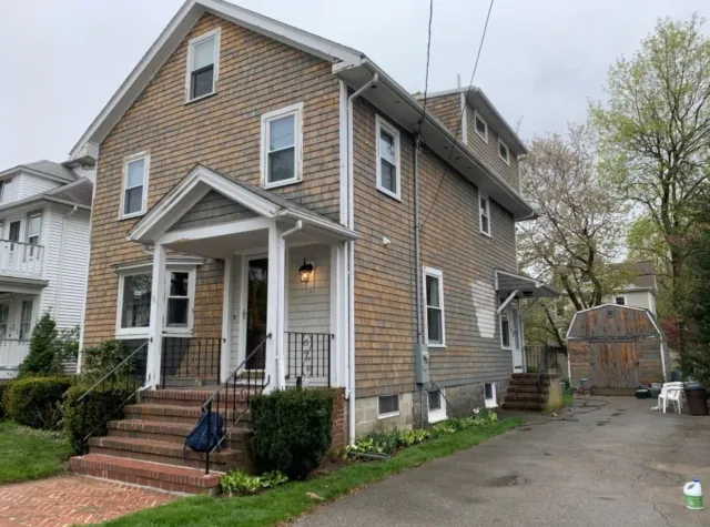 Brick two-story house with front porch and driveway, viewed from the side on a cloudy day