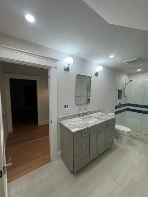 Modern bathroom with gray vanity, marble countertop, mirror, wall lights, and striped shower curtain.