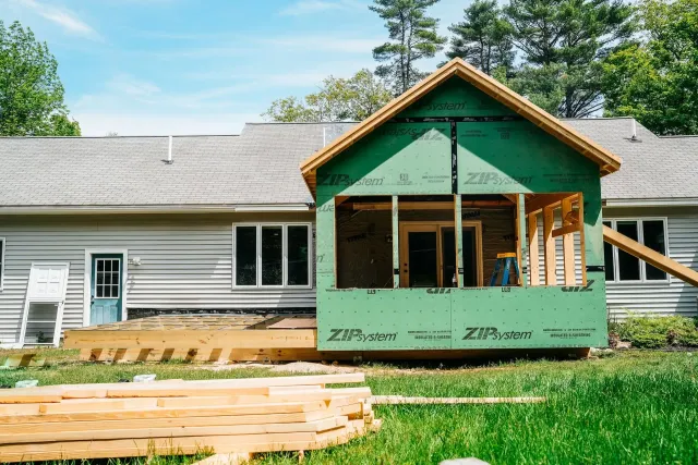 House under renovation with green front porch framing and exposed construction materials in front
