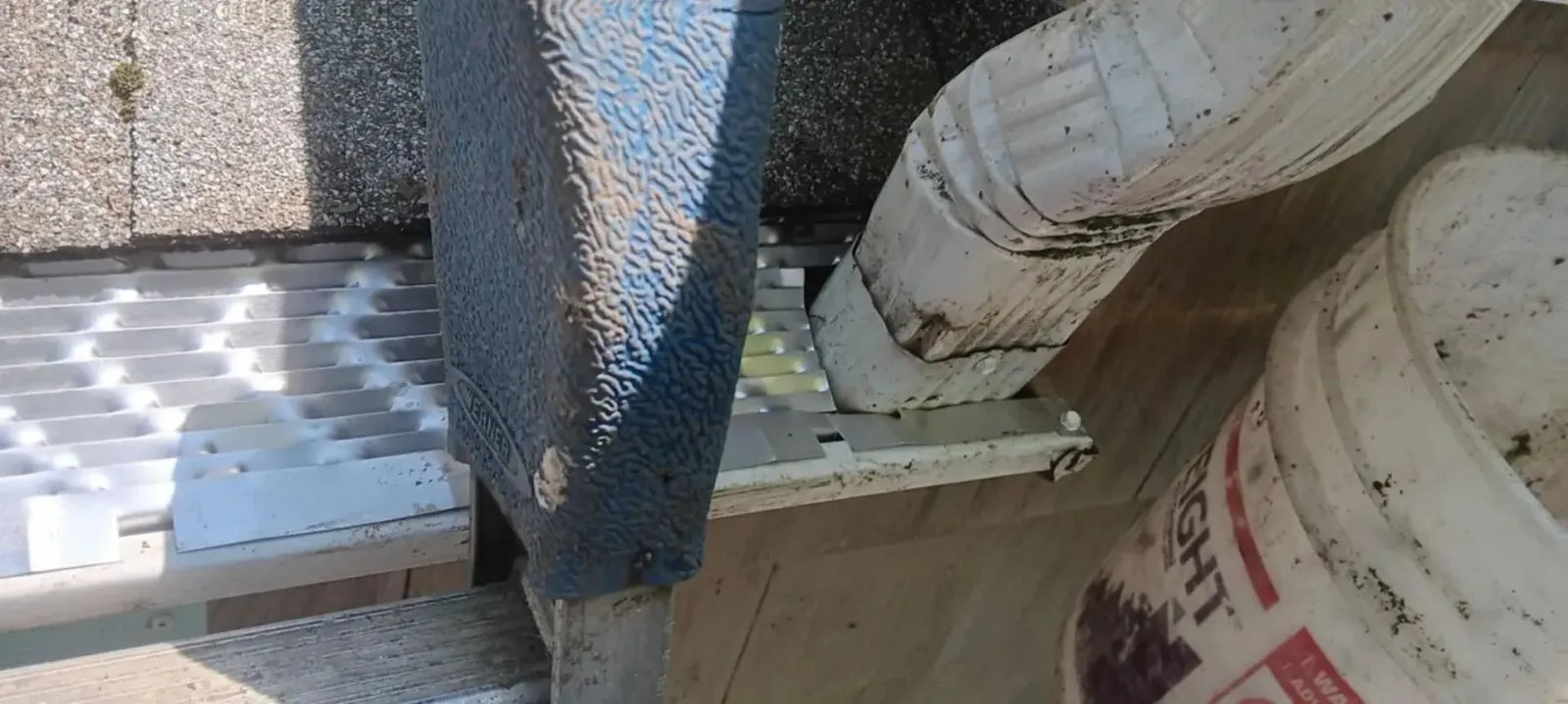 Construction materials stacked on a site beside a blue mesh barrier and white buckets