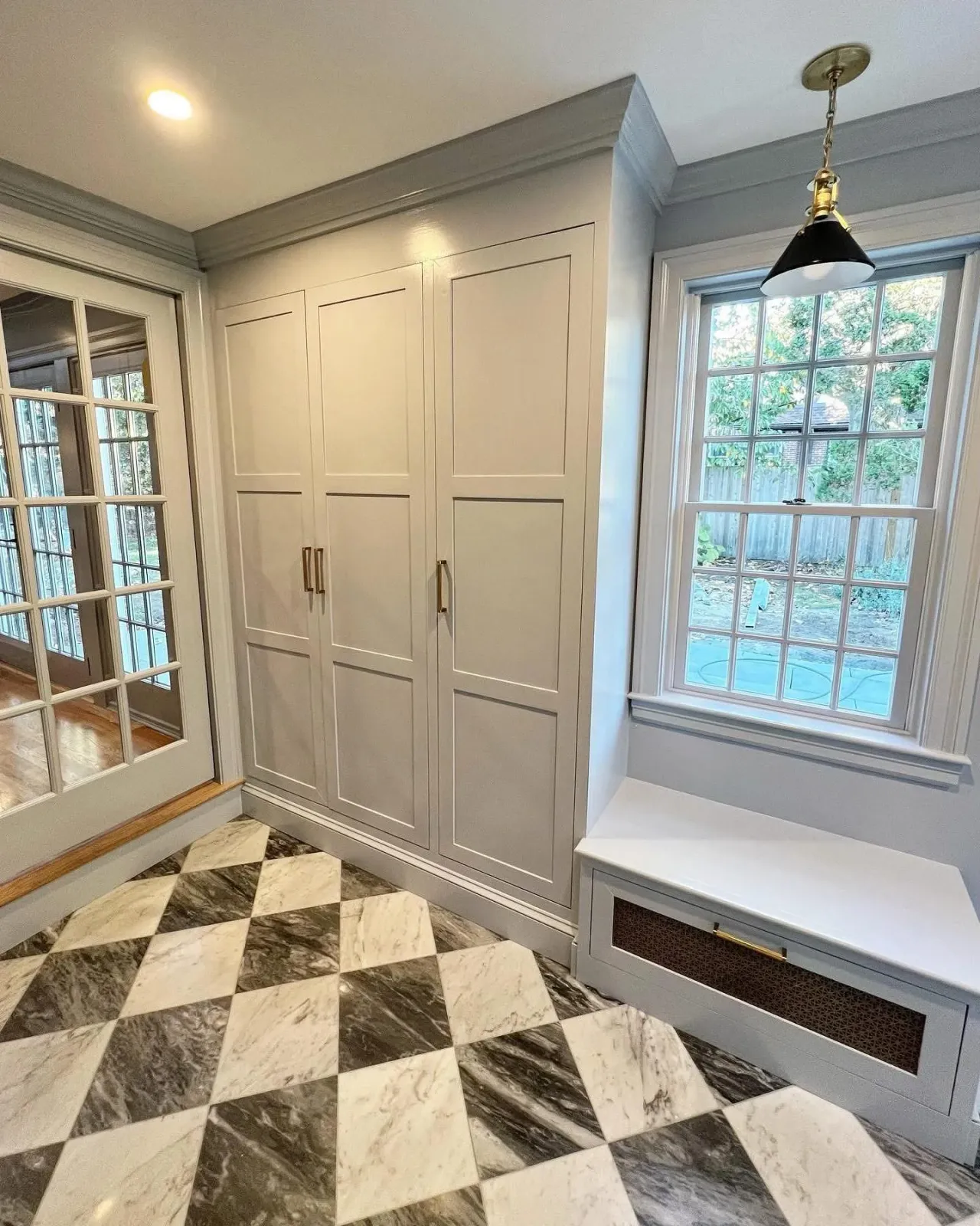 Corner of a room with white cabinetry, a window showing a backyard, and a black pendant light.