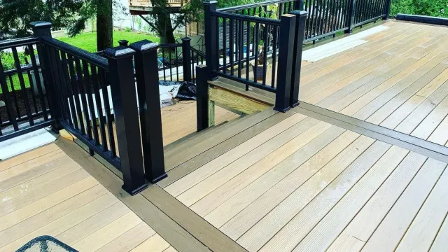 A wooden deck with a black railing and stairs leading up to it.