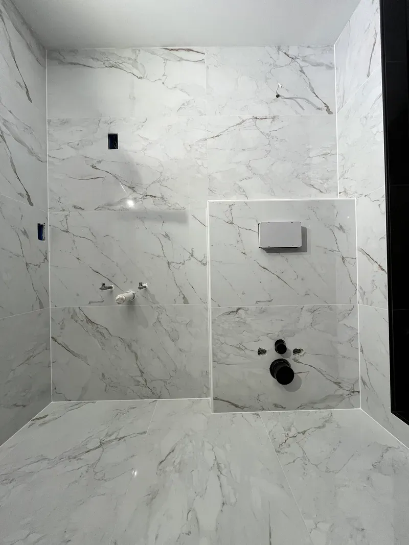 Full wall of large-format marble-look porcelain with 1/16 inch joints and the tiled access panel framed in