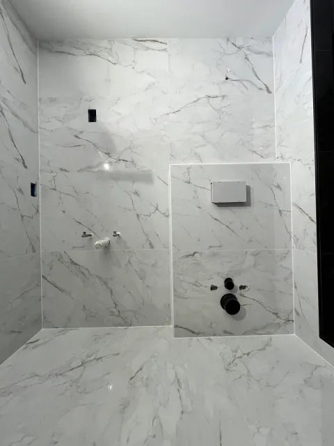 Full wall of large-format marble-look porcelain with 1/16 inch joints and the tiled access panel framed in