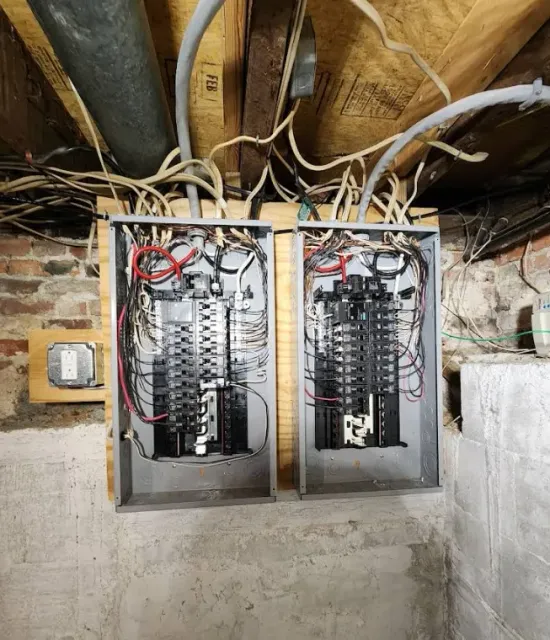 Two electrical panels are hanging from the ceiling in a basement