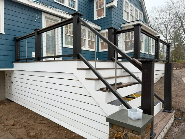 Custom exterior staircase with white risers, black posts, and wire cable railings on a blue house.