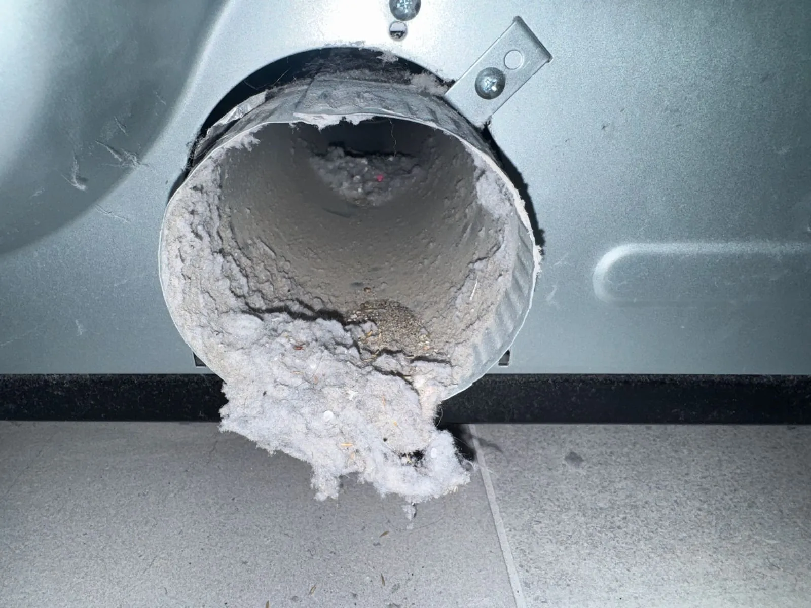 Flexible dryer duct disconnected at the appliance, its open end ringed with a thick collar of packed lint.